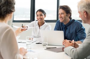 Cheerful businesswoman giving report to senior manager. Happy businessmen and businesswomen in a meeting. Young marketing manager handing over report of month sales to executive.